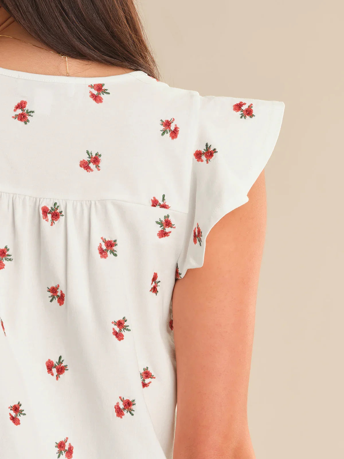 White top with red floral patterns on a beige background