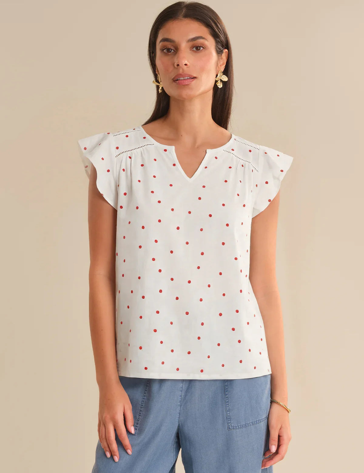Woman wearing a white blouse with red polka dots and blue pants on a beige background