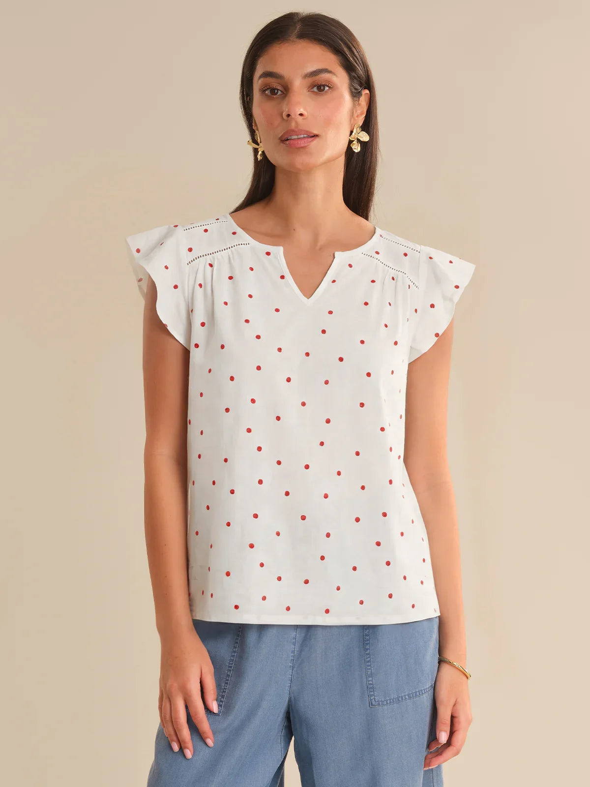 Woman wearing a white blouse with red polka dots and blue pants on a beige background