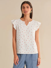 Woman wearing a white blouse with red polka dots and blue pants on a beige background