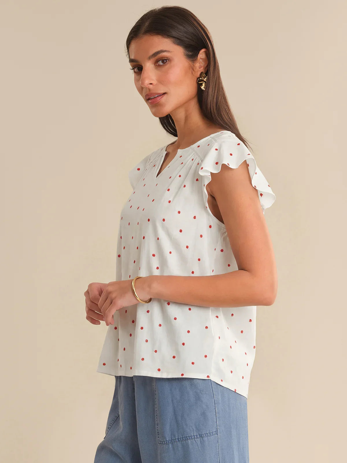 Woman wearing a white blouse with red polka dots and blue pants on a beige background