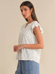 Woman wearing a white blouse with red polka dots and blue pants on a beige background