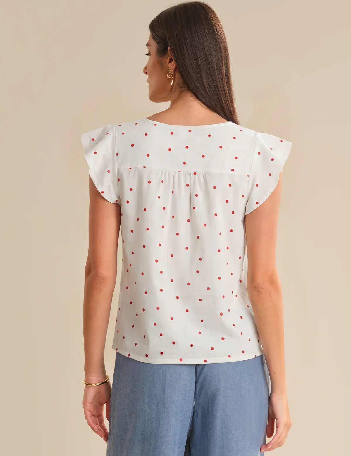 Woman wearing a light red polka dot top and blue pants on a beige background