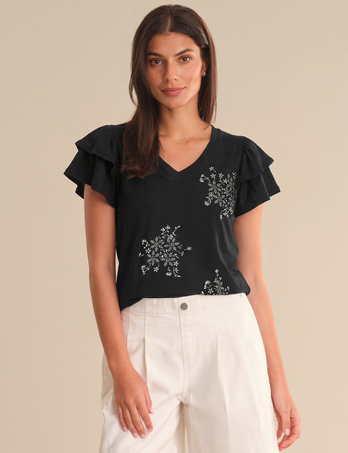 Woman wearing a black top with floral embroidery and white pants on a beige background