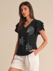 Woman wearing a black top with floral embroidery and white shorts on a beige background