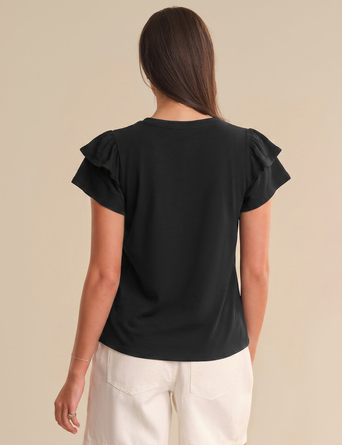 Woman wearing a black top with ruffled sleeves on a beige background