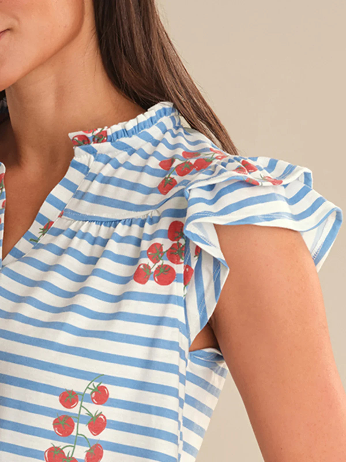 Woman wearing a blue and white striped top with tomato designs on a neutral background