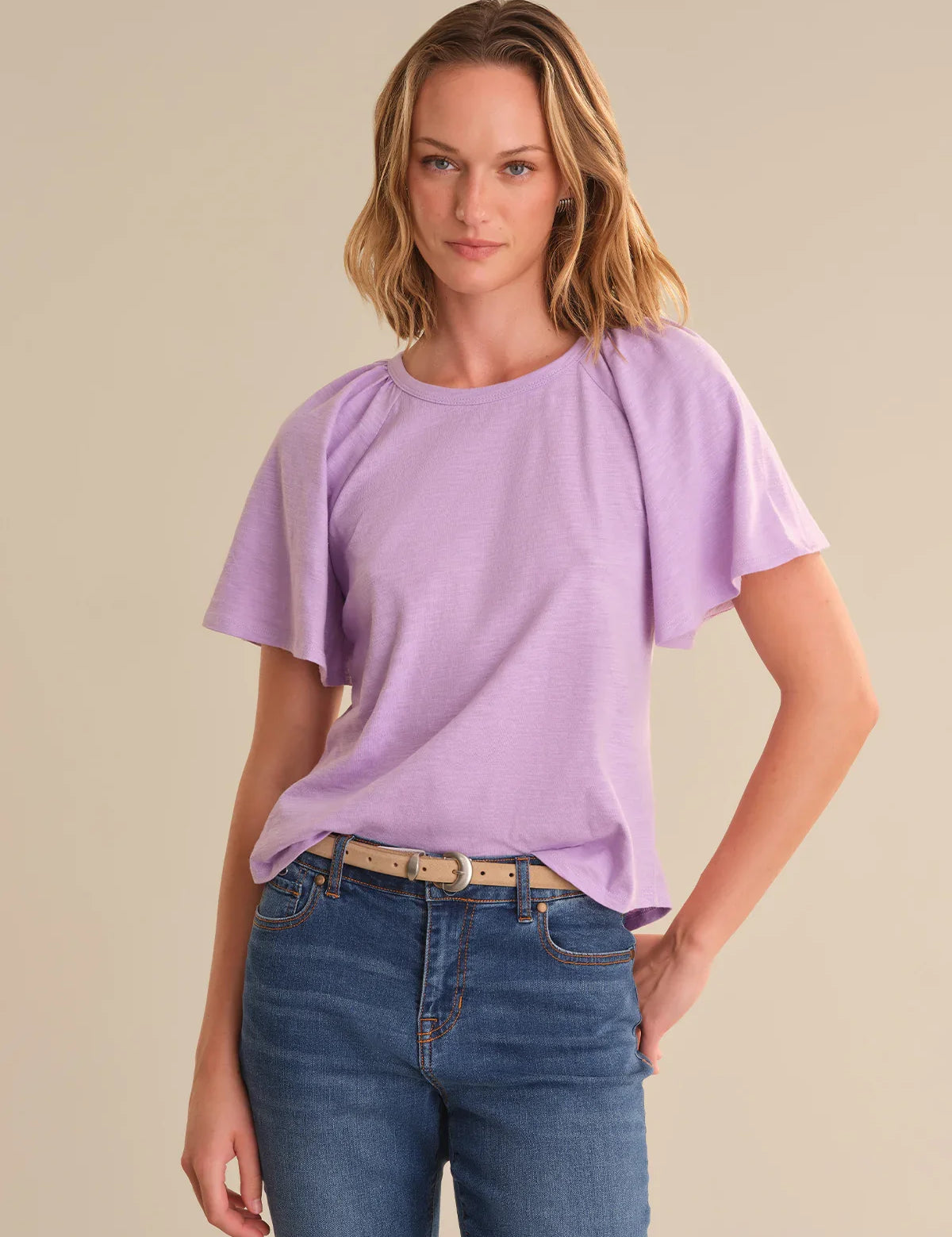 Woman wearing a light purple top and blue jeans on a beige background