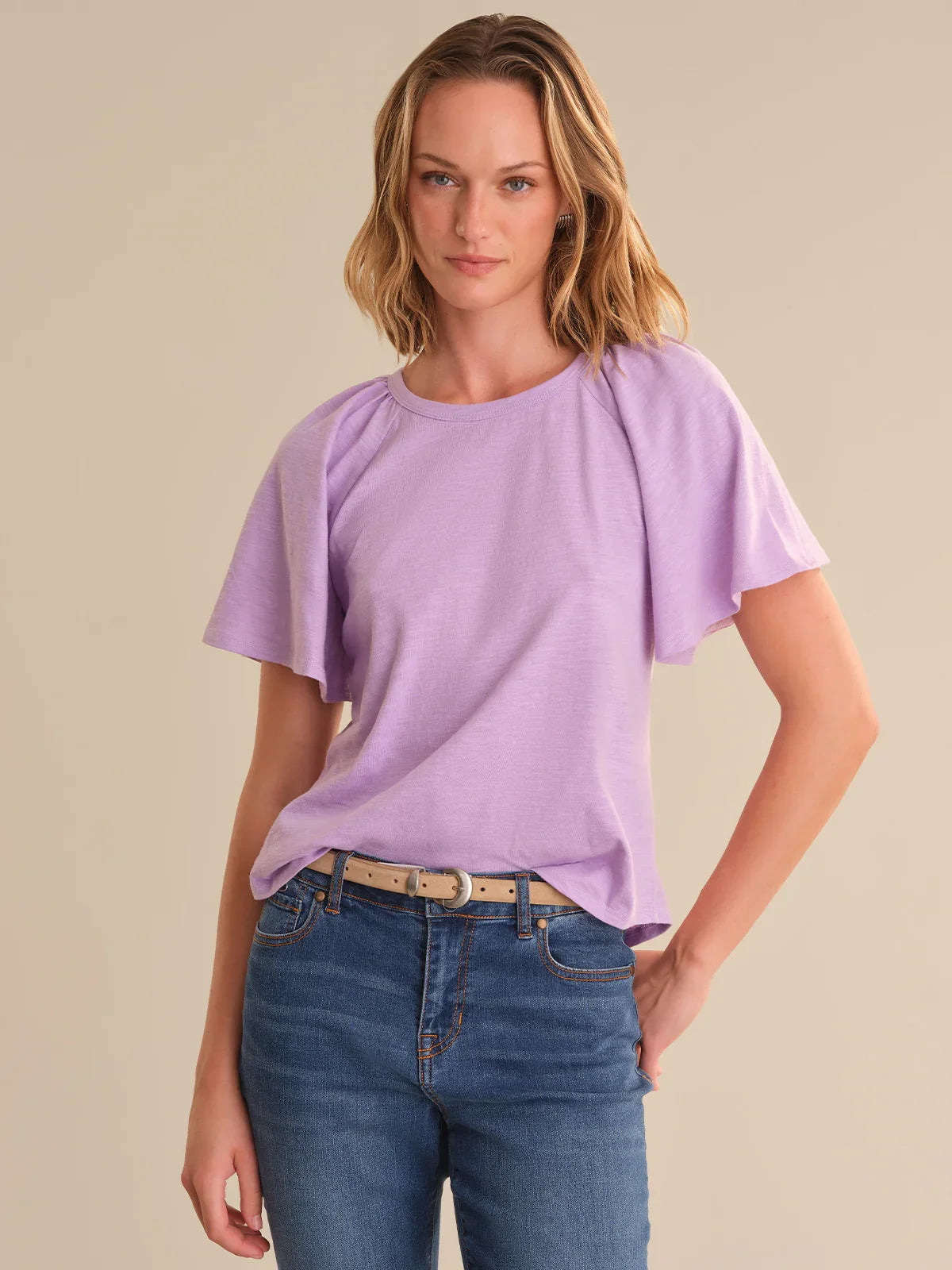Woman wearing a light purple top and blue jeans on a beige background
