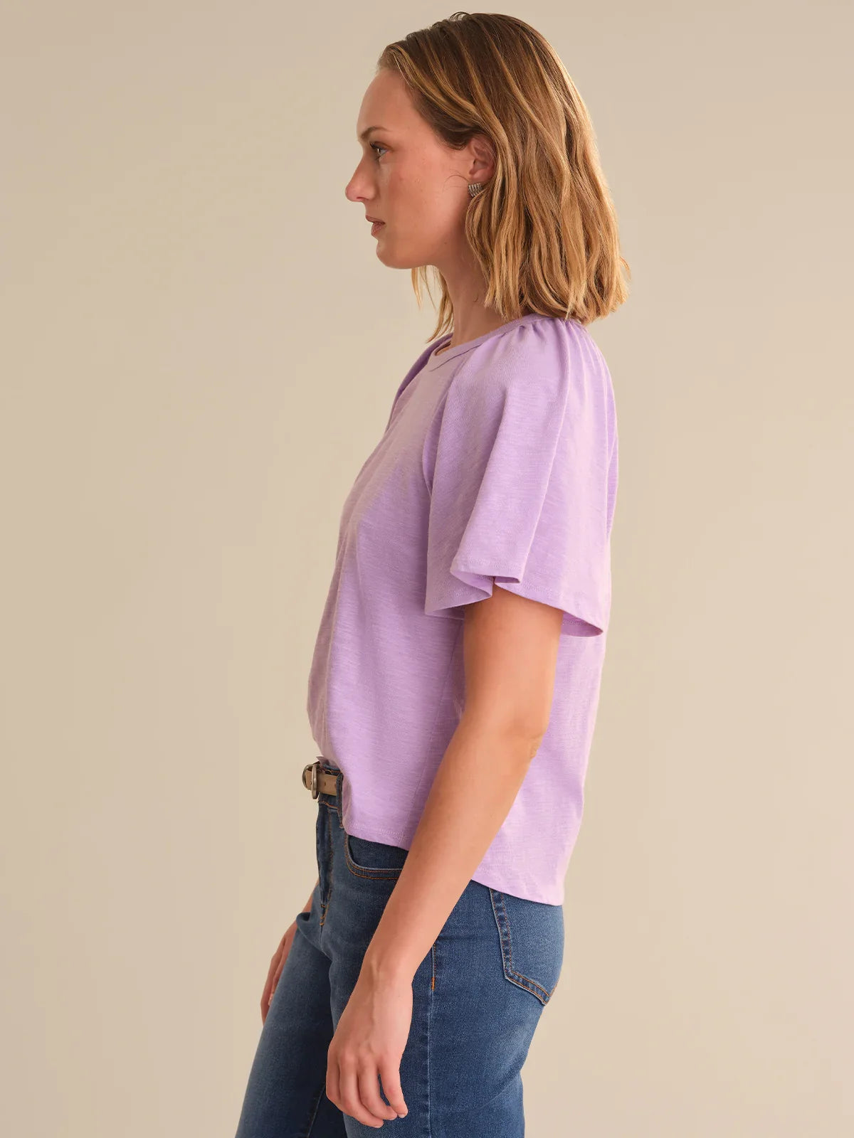 Woman wearing a light purple top and blue jeans against a beige background