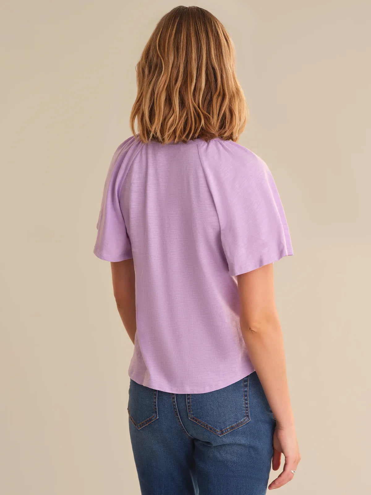 Person wearing a light purple t-shirt and blue jeans on a beige background