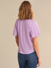 Person wearing a light purple t-shirt and blue jeans on a beige background
