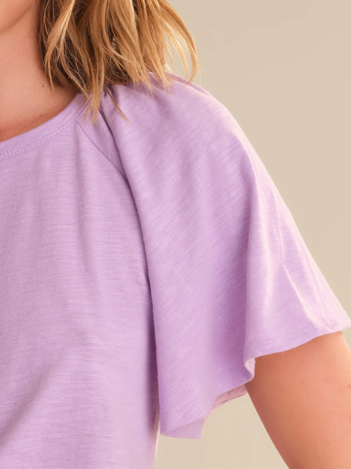 Close-up of a person wearing a light purple top against a neutral background