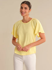Woman wearing a yellow top and white pants against a beige background