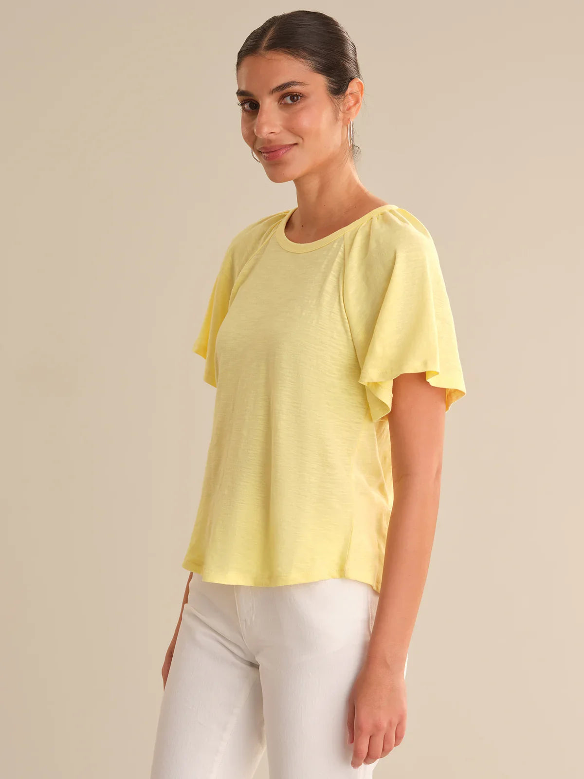 Woman wearing a yellow top with ruffled sleeves on a beige background