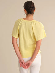 Woman wearing a yellow top and white pants against a beige background