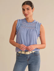 Woman wearing a blue sleeveless top with ruffled details and jeans on a beige background