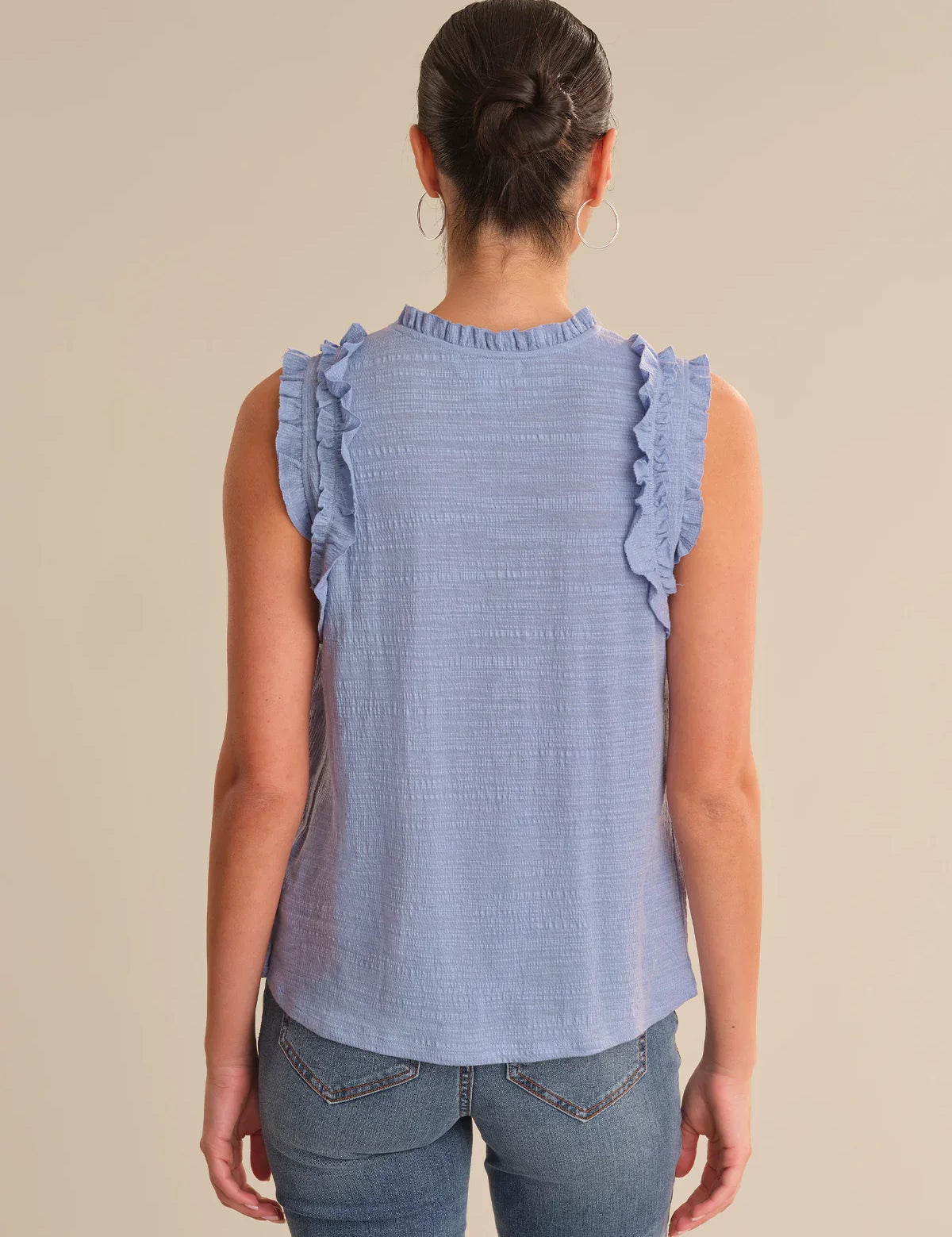 Woman wearing a blue sleeveless top with ruffled details on a beige background