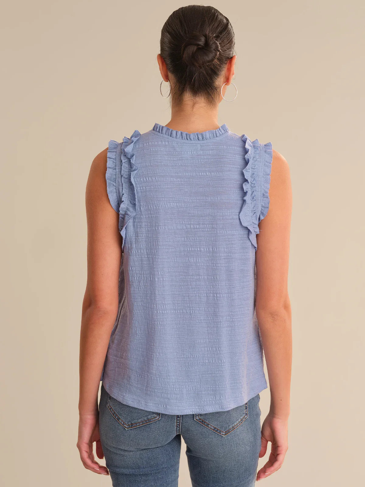 Woman wearing a blue sleeveless top with ruffled details on a beige background