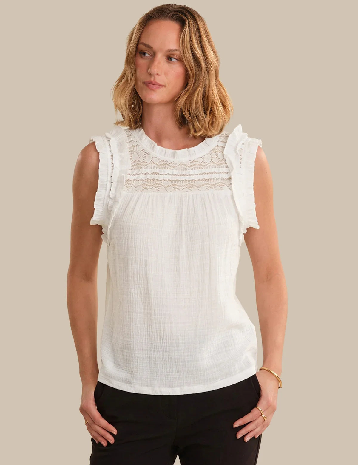 Woman wearing a white sleeveless top with lace details on a beige background