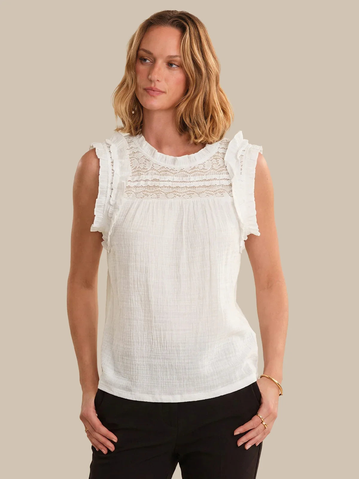 Woman wearing a white sleeveless top with lace details on a beige background