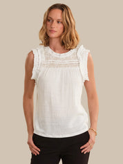 Woman wearing a white sleeveless top with lace details on a beige background