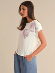 Woman wearing a white t-shirt with floral design and blue pants on a beige background