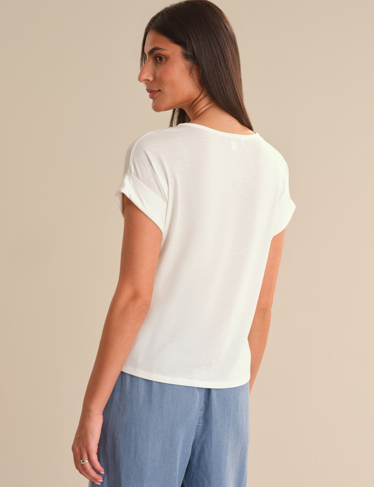 Woman wearing a white t-shirt and blue pants against a beige background
