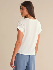 Woman wearing a white t-shirt and blue pants against a beige background