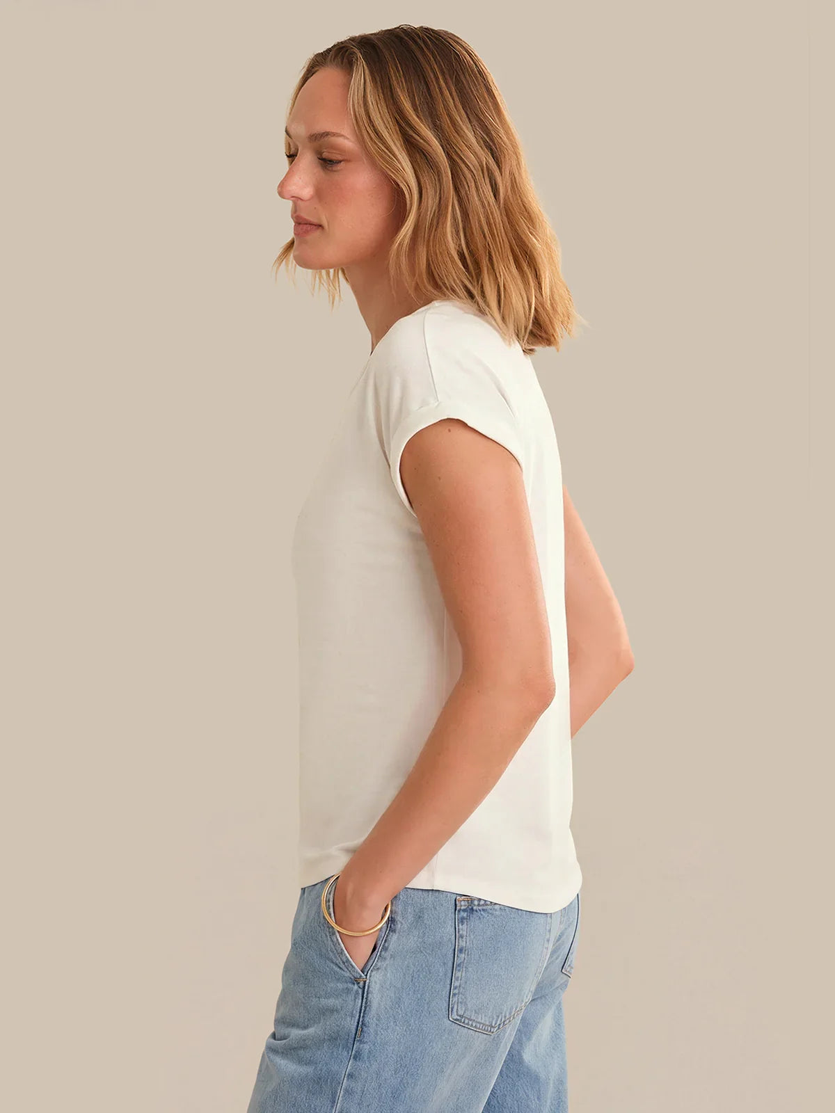 Woman wearing a white t-shirt and blue jeans against a plain background