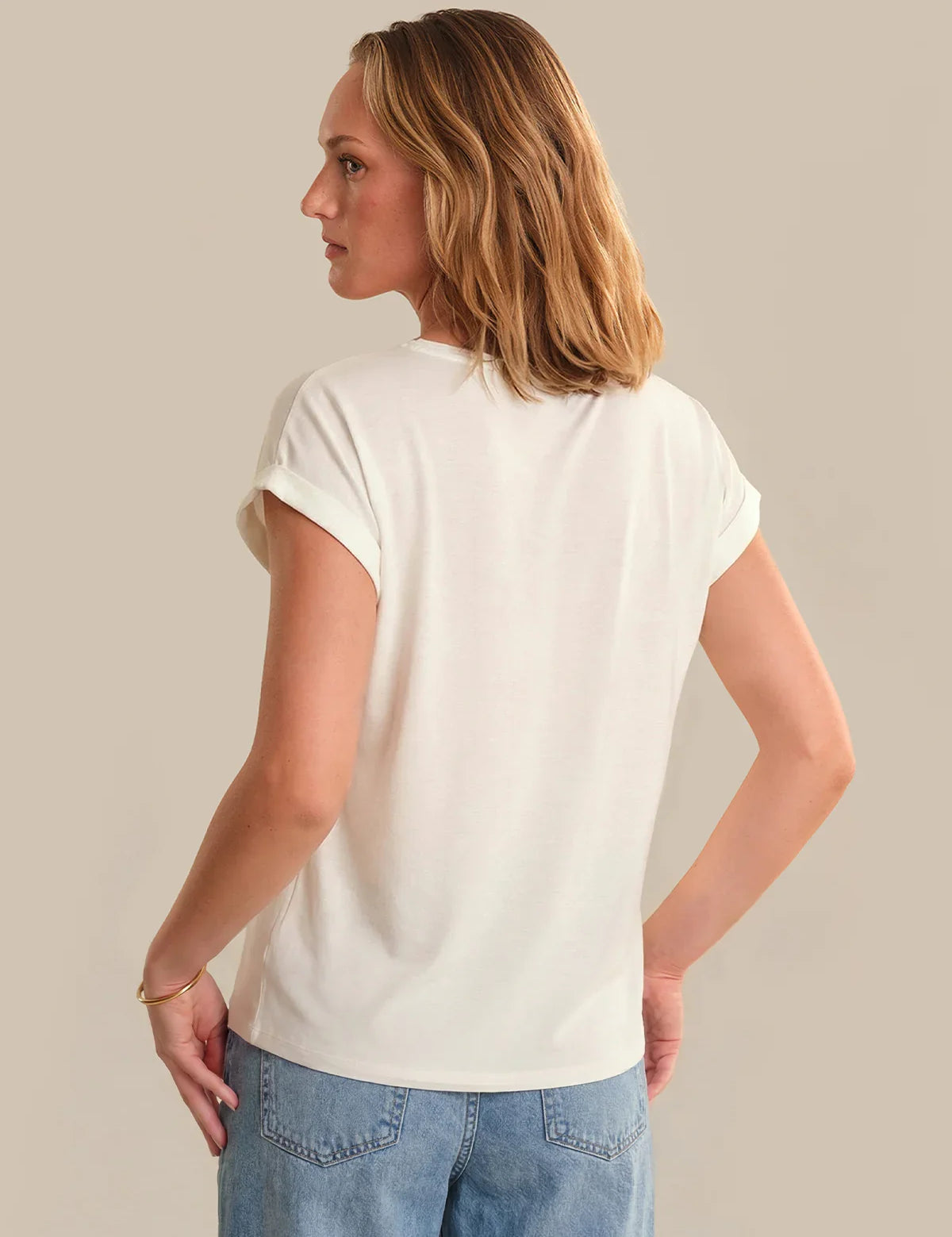 Woman wearing a plain white t-shirt and blue jeans against a neutral background