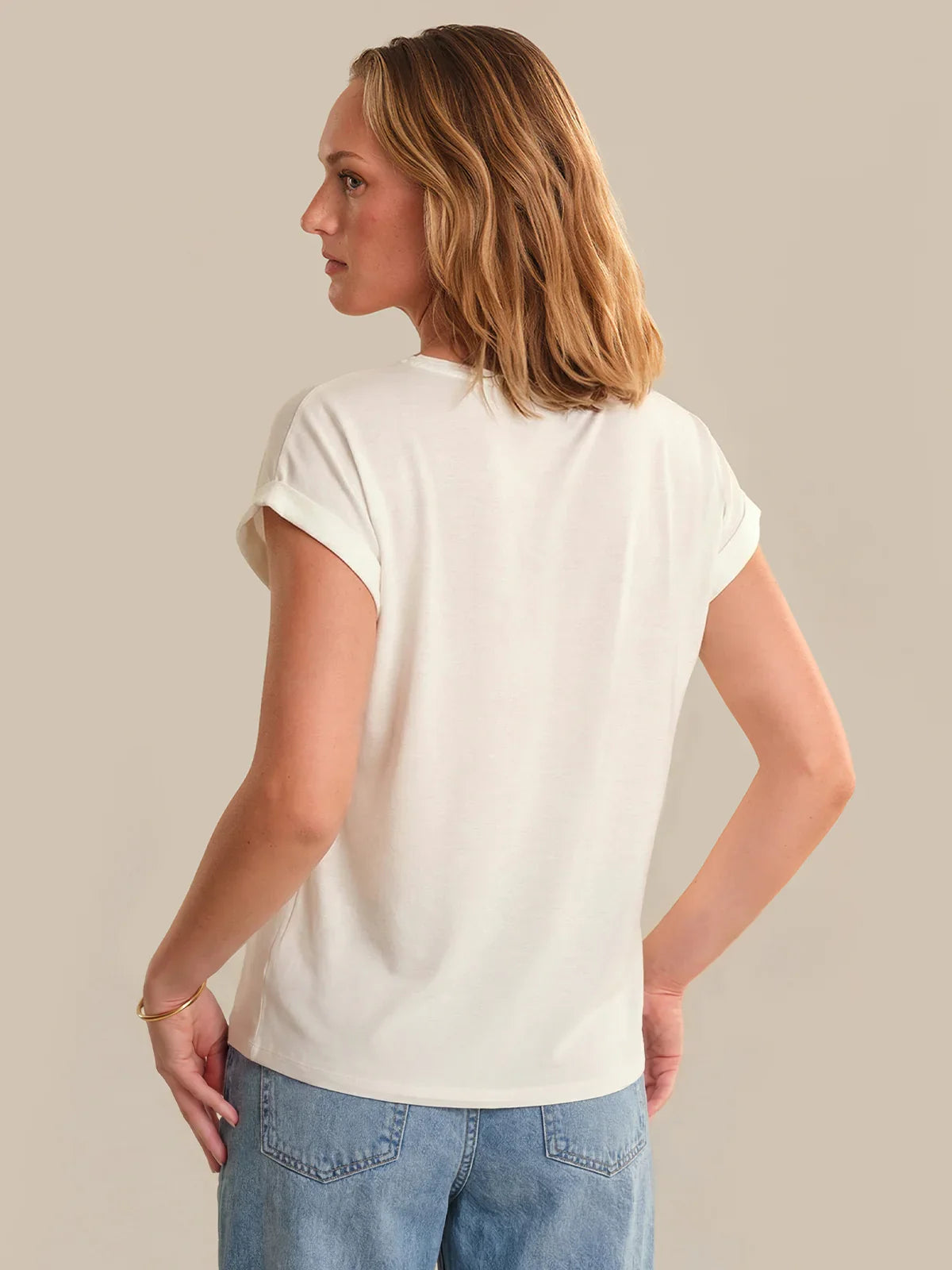 Woman wearing a plain white t-shirt and blue jeans against a neutral background