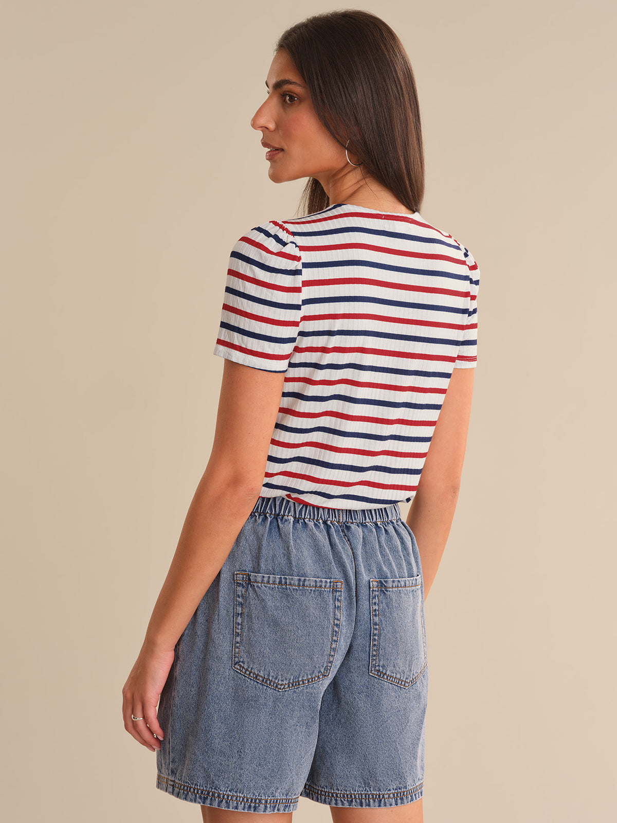 Woman wearing a striped shirt and denim shorts on a beige background
