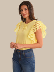 Woman wearing a yellow blouse with lace details and blue jeans on a beige background