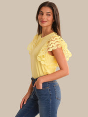 Woman wearing a yellow lace top and blue jeans on a beige background