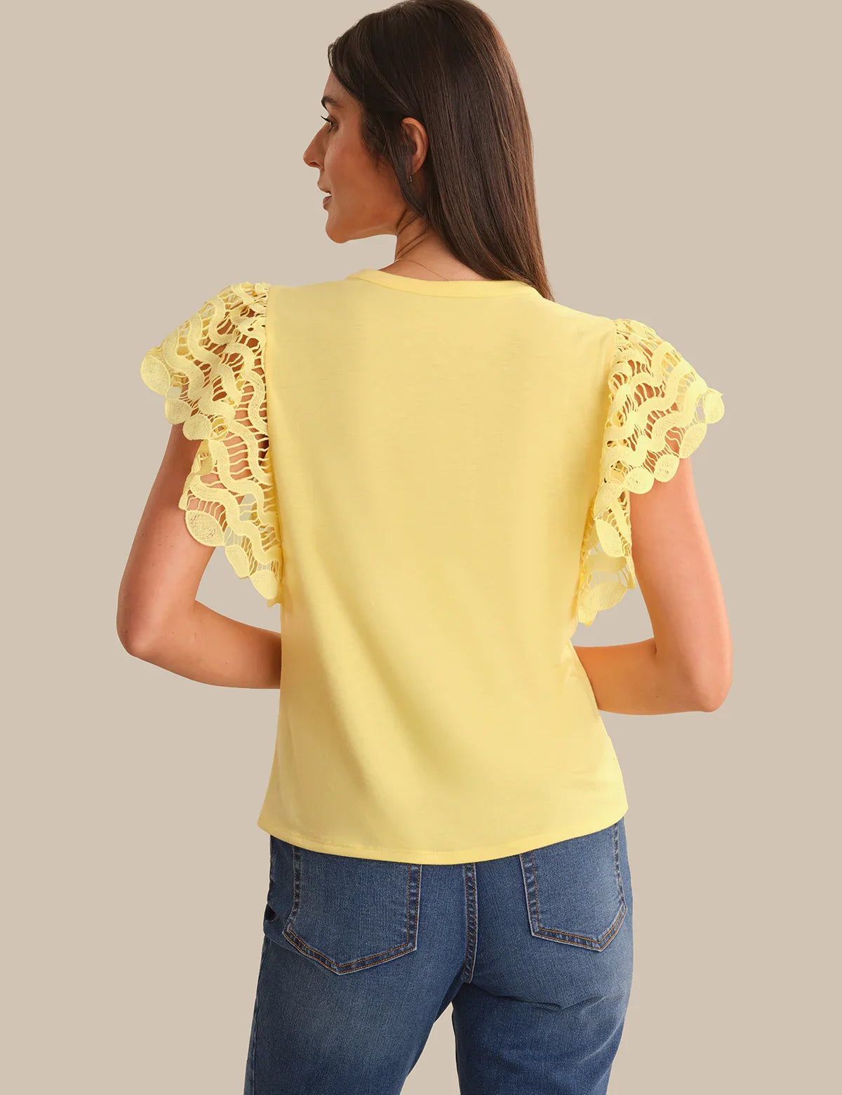 Woman wearing a yellow top with lace sleeves on a beige background