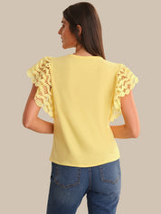 Woman wearing a yellow top with lace sleeves on a beige background