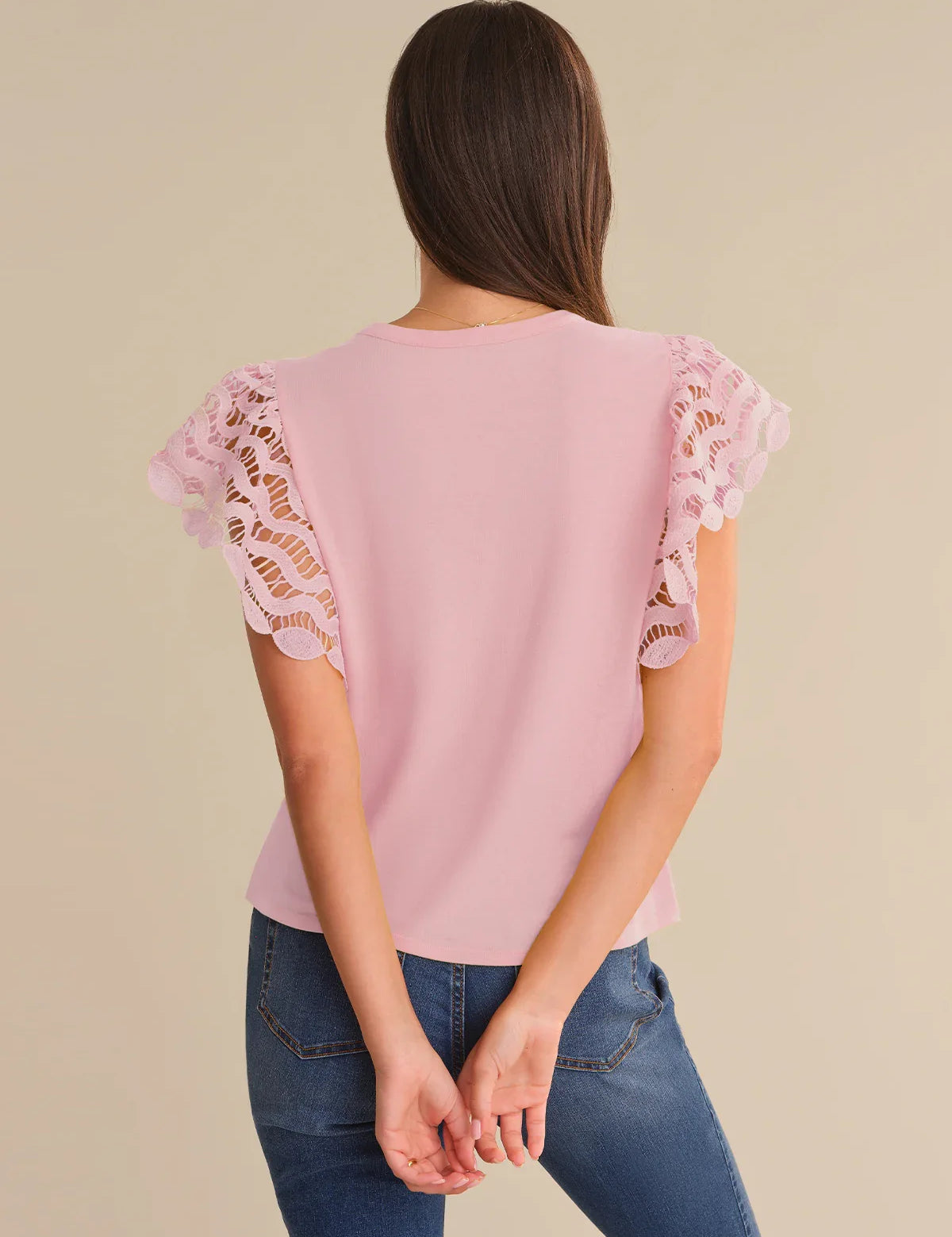 Pink blouse with lace sleeves worn by a person on a beige background