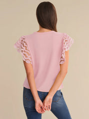 Pink blouse with lace sleeves worn by a person on a beige background