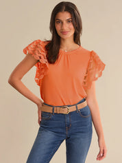 Woman wearing an orange top with lace sleeves and blue jeans on a beige background