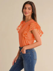 Woman wearing an orange lace top and blue jeans on a beige background