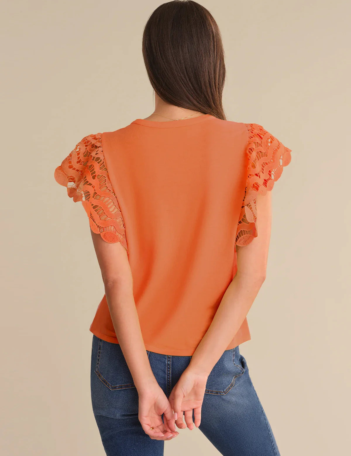 Orange top with lace sleeves worn by a person on a beige background