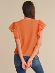 Orange top with lace sleeves worn by a person on a beige background