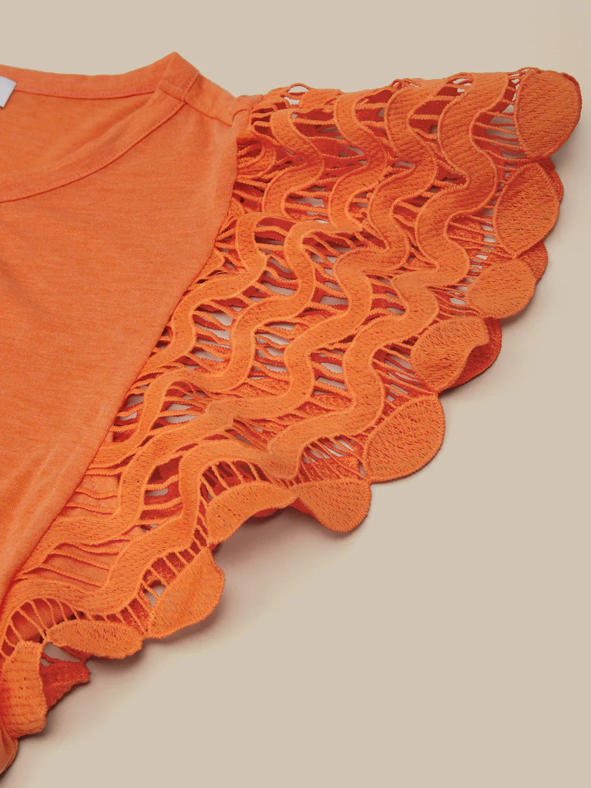 Orange top with intricate lace detailing on a beige background