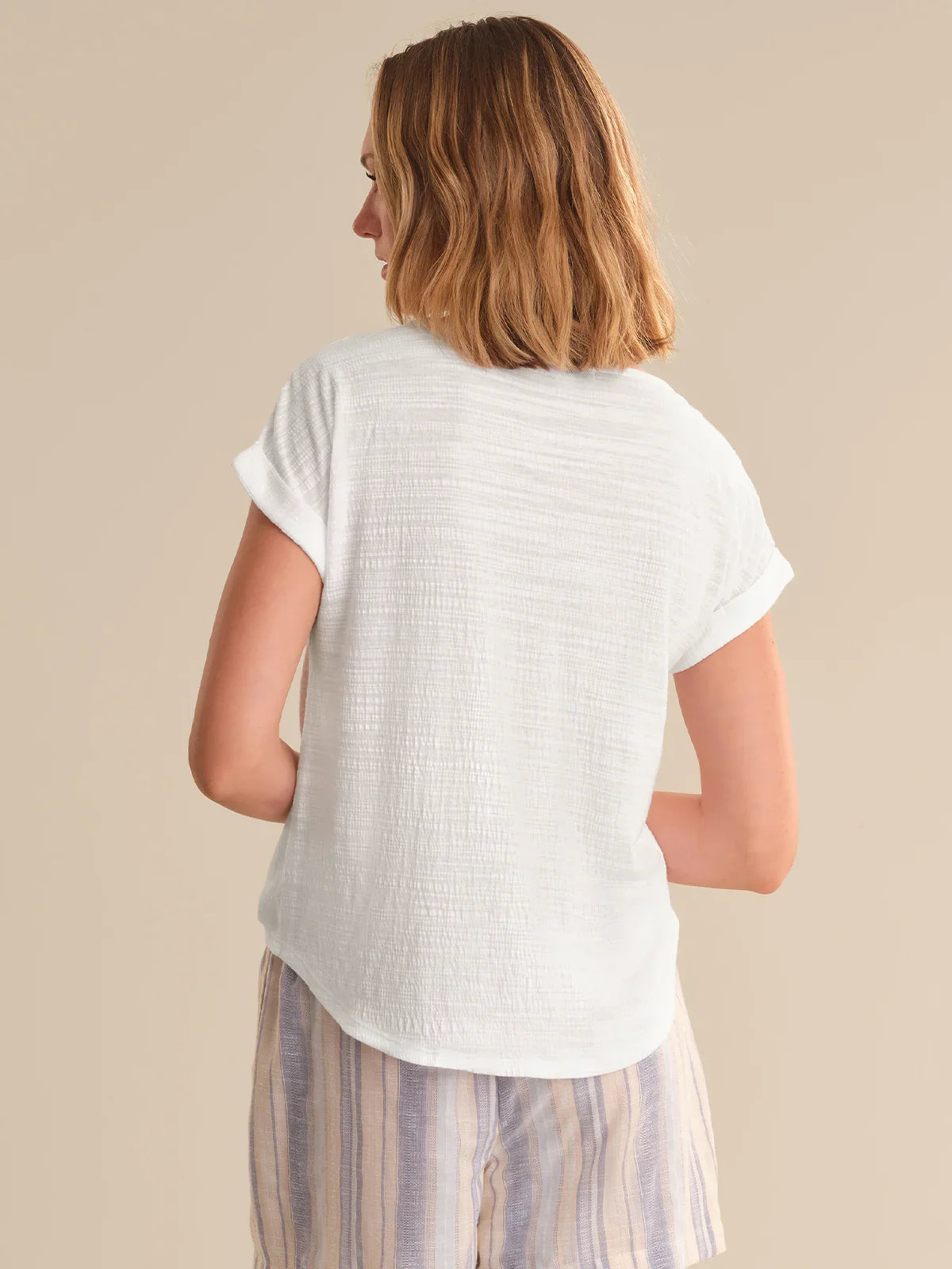 Woman wearing a white textured shirt and striped pants against a beige background