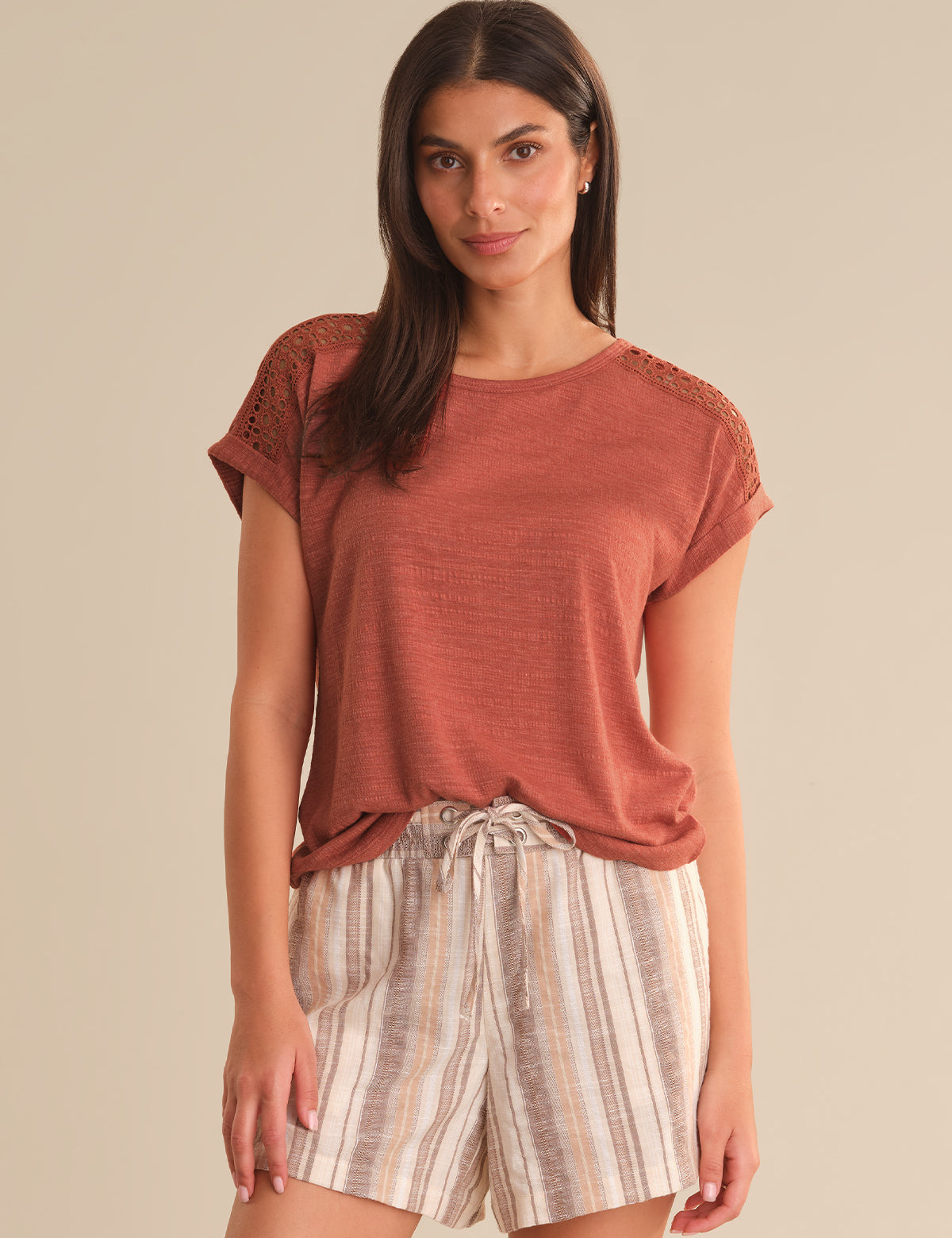 Woman wearing a rust-colored top and striped shorts on a beige background
