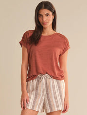 Woman wearing a rust-colored top and striped shorts on a beige background