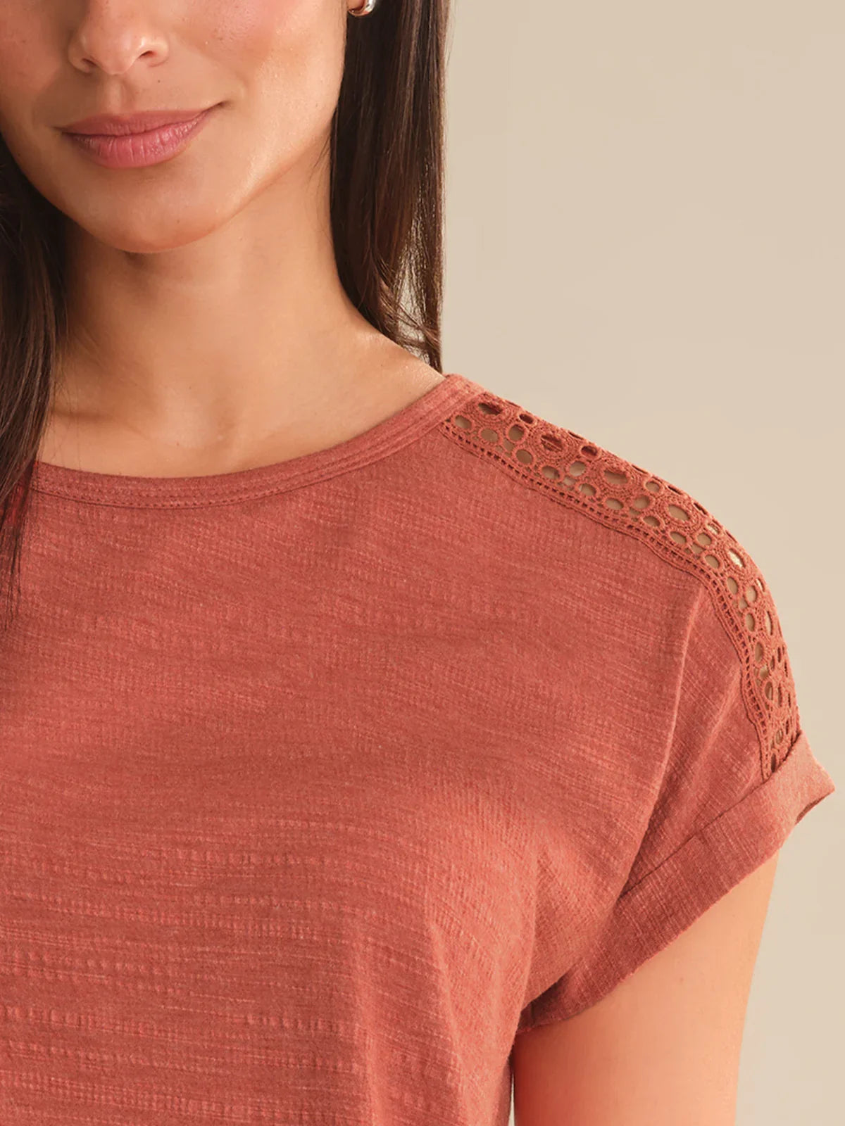 Close-up of a person wearing a rust-colored top with lace details on a beige background