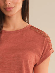 Close-up of a person wearing a rust-colored top with lace details on a beige background