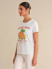 Woman wearing a white t-shirt with 'Amalfi Coast' graphic design on a beige background